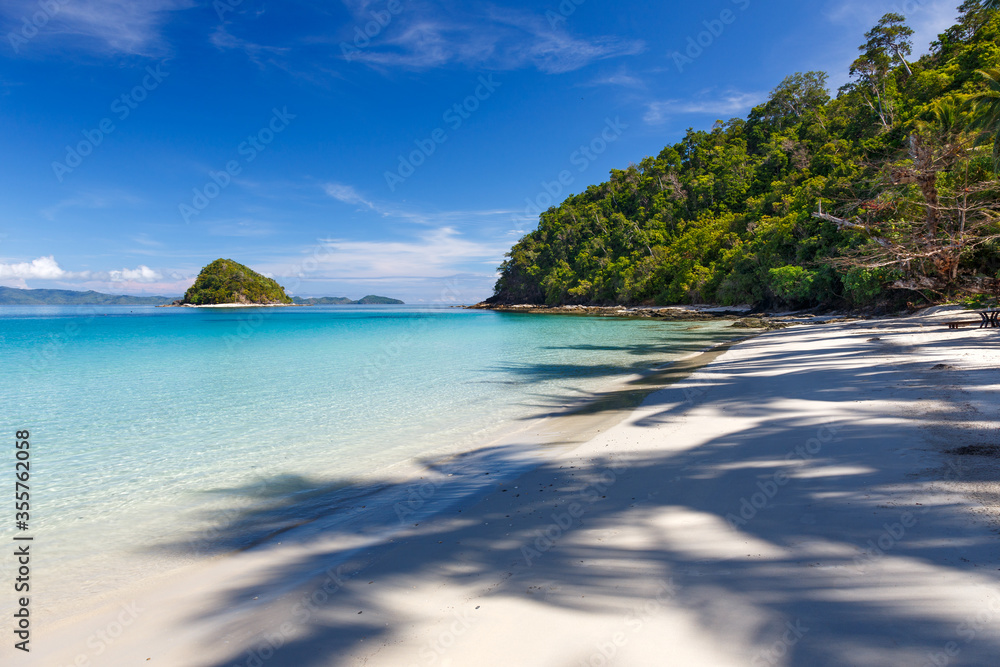 Fototapeta premium Tropical beach with white sand and a shadow of coconut trees on it. A Paradise for relaxation, Islands on the horizon, clear sea water.
