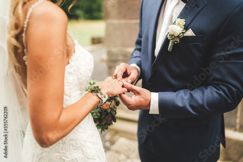 Close up of groom putting wedding ring on bride's finger. Bride and groom holding hands at wedding ceremony. Wedding rings on newlyweds hands.