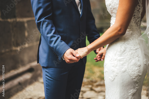 Young adult groom and bride holding hands. Outdoor photo. Wedding day concept.