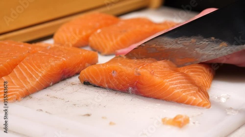 Cutting raw salmon fillet on a white chopping board. Preparing fish steak for cooking in the kitchen.