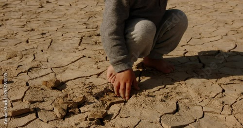 Close up shot of baby boy poking pieces of dry cracked mud. Cracked soil ground of dried lake or river destroyed ny global warming - ecological issues 4k footage