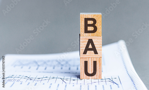 Word BAU - business as usual - acronym concept on cubes and diagrams on a gray background. Business As Usual concept image.
