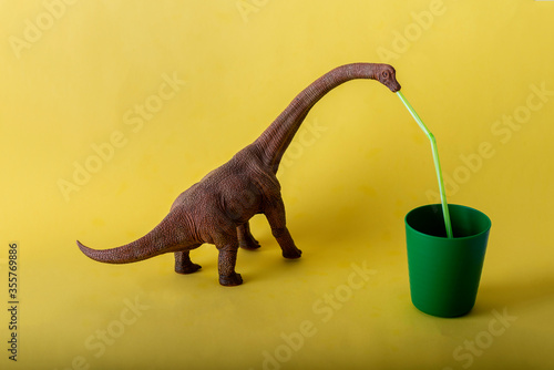 Dinosaurio Herb  voro bebiendo de un vaso de pl  stico verde con una pajita en un fondo amarillo