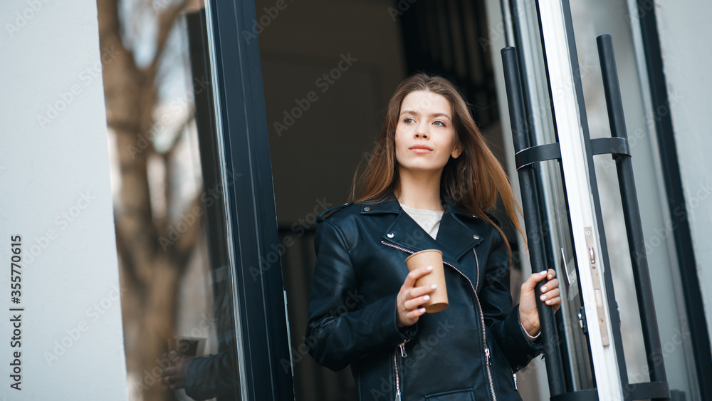 Young woman going out of urban building through a large glass door Young woman going out of urban building through a large glass door