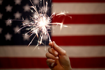 Hand holding lit sparkler in front of the American Flag for 4th of July celebration