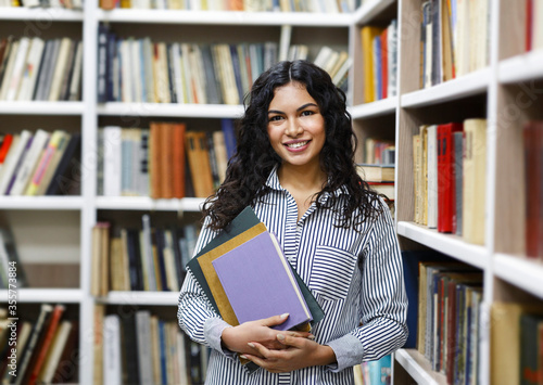 фотографія Smiling latina girl holding textbooks at library