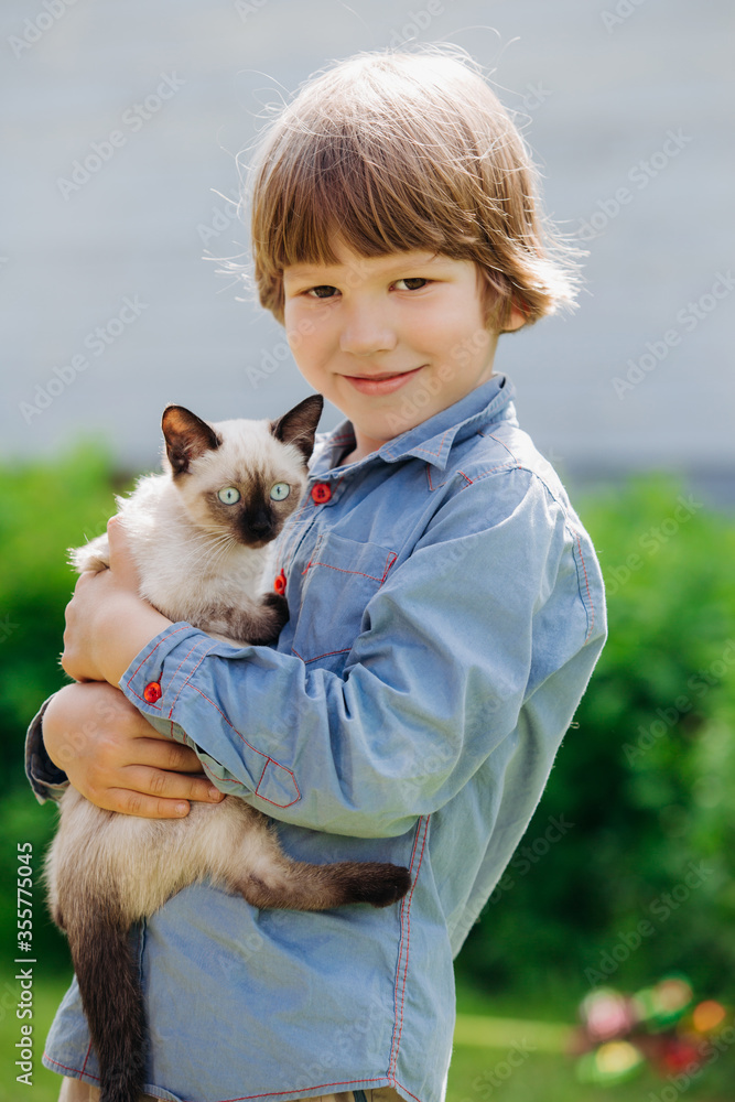 Kid plays in the summer outdoors. Сhild is friends with pet in summertime. Cute toddler is playing with a kitten on grass. Boy and baby cat Kid plays in the summer outdoors. Сhild is friends with pet in summertime. Cute toddler is playing with a kitten on grass. Boy and baby cat