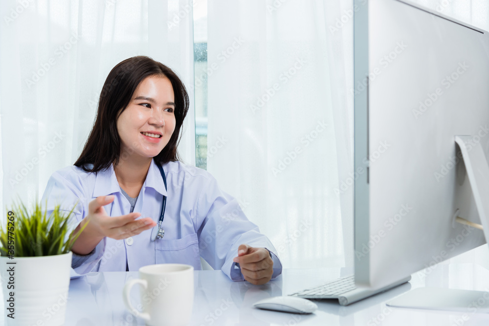 Asian young beautiful woman doctor video call conference online raise hand to explain to patients on front desktop PC computer monitor quarantines disease coronavirus or COVID-19 at hospital office Asian young beautiful woman doctor video call conference online raise hand to explain to patients on front desktop PC computer monitor quarantines disease coronavirus or COVID-19 at hospital office