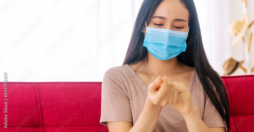 Hands of young woman wearing face mask using alcohol gel washing hand before working while sitting on sofa at home. Female using antiseptic alcohol hand gel clean sanitizer for killing virus in hand.