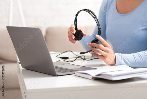 Beginning of working day of online consultant. Woman holds headphones in her hands, near laptop and notebook on table