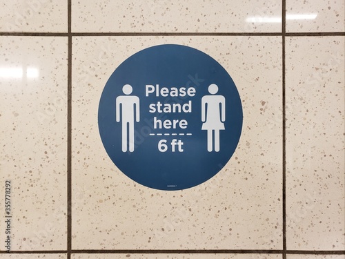 Please stand six feet apart and social distance signs in blue and white are displayed on a tile floor due to COVID-19 as businesses and retail establishments begin to reopen. photo