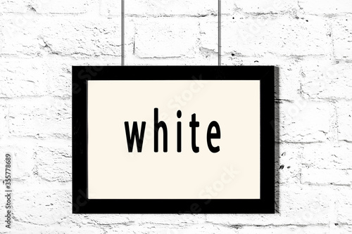 Black frame hanging on white brick wall with inscription white Fototapeta