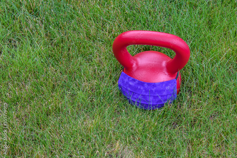 Red kettle bell with a purple face mask, on a green lawn, ready for an outdoor workout
Red kettle bell with a purple face mask, on a green lawn, ready for an outdoor workout