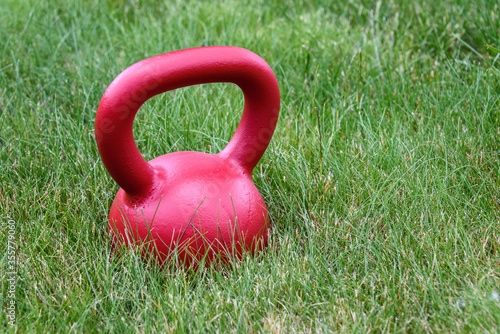 Fototapeta Naklejka Na Ścianę i Meble -  Red kettle bell on a green lawn, ready for an outdoor workout
