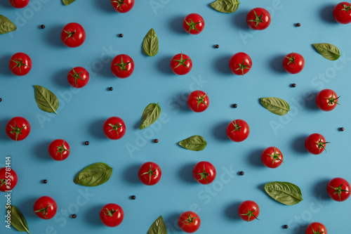 Fresh organic red tomatoes, peppercorns and basil leaves on blue background. Vegetables harvested for making salad. Healthy eating and vitamins concept. Horizontal shot, top view. Tasty natural food