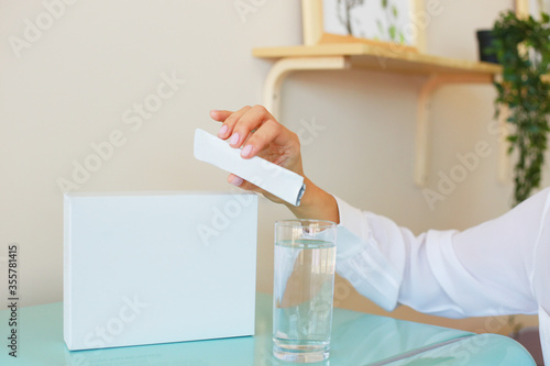 Woman pours the contents of a sachet into a glass. Universal stick pack for products of the food, pharmaceutical, cosmetic and chemical industry.