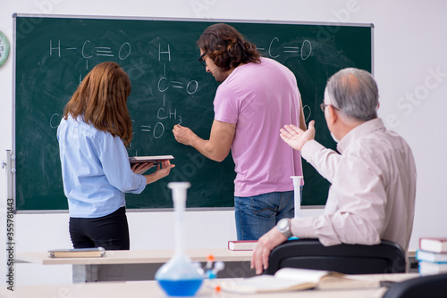 Old chemist teacher and two students in the classroom