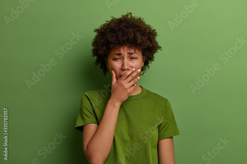 Upset stressful woman in despair, feels depressed, sobs or whins loudly, cannot stop crying, faces troublesome situation, stands grieved against vibrant green background. Negative emotions concept