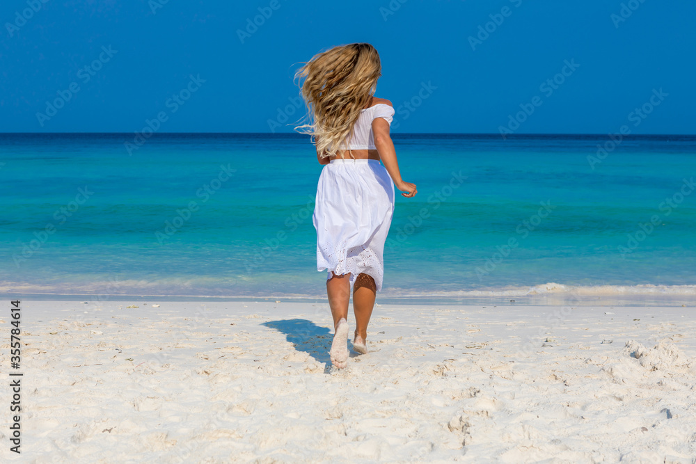 Young beautiful girl in white clothes walks along the sandy beach near the water