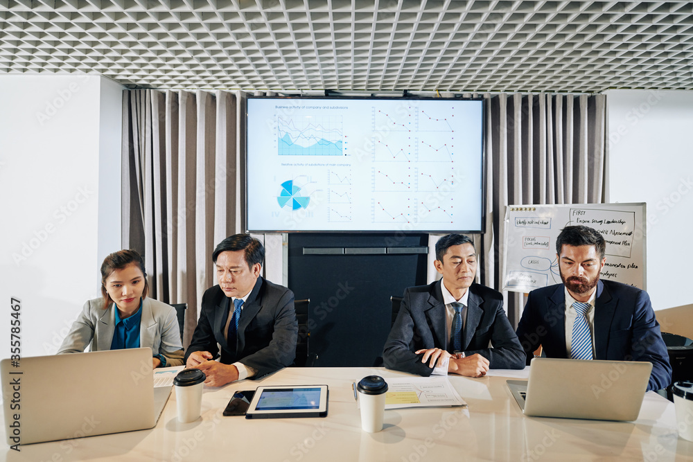 Managers of finance department discussing charts and diagrams of income during pandemic period at meeting Managers of finance department discussing charts and diagrams of income during pandemic period at meeting
