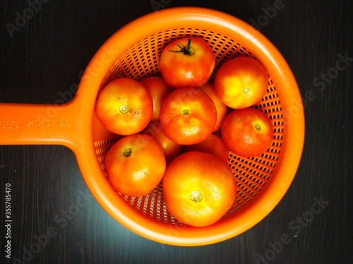 A shot from top of a group of fresh tomatoes arranged in a proper arrangement in a orange coloured bowl with good lighting method