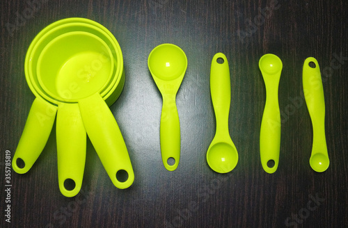 A close up shot of a set of green colour measurement cups and spoon arranged under a proper lighting. The measurement cups and spoons are widely used in baking to achieve the precise amount.