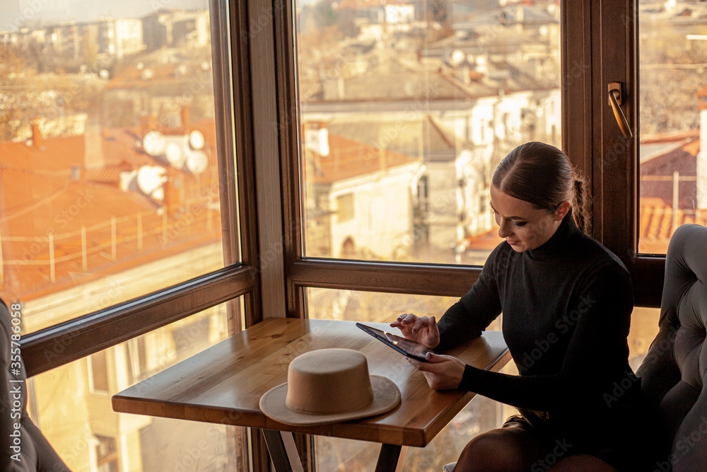 Female sitting in cafe on the roof of the city and using a laptop. Fashion woman dressed style black golf. Freelancer relexing on the rooftop and holding computer. Female sitting in cafe on the roof of the city and using a laptop. Fashion woman dressed style black golf. Freelancer relexing on the rooftop and holding computer.