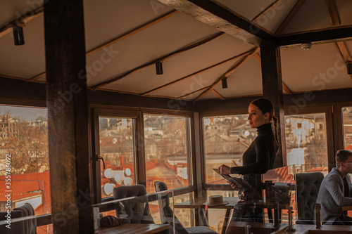 Female posing in cafe on the roof of the city and using a laptop. Fashion woman dressed style black golf and shorts. Freelancer relexing on the rooftop and holding computer.