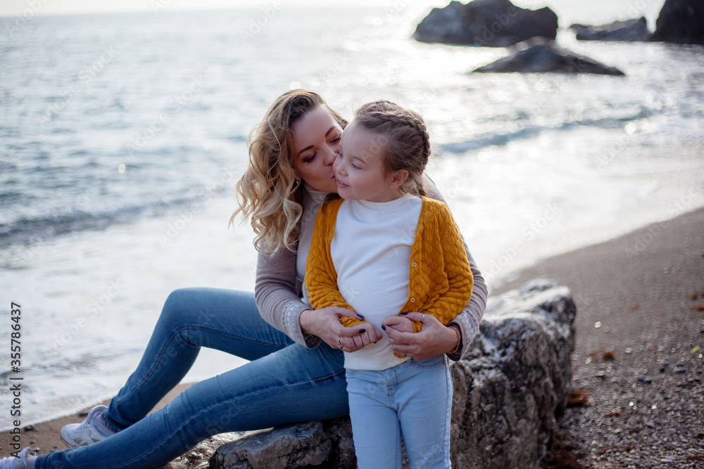 Happy family posing outdoor in the beach of the sea at spring time. woman with daughter have fun on vacation near ocean.  Travel, love, holidays concept - lifestyle
