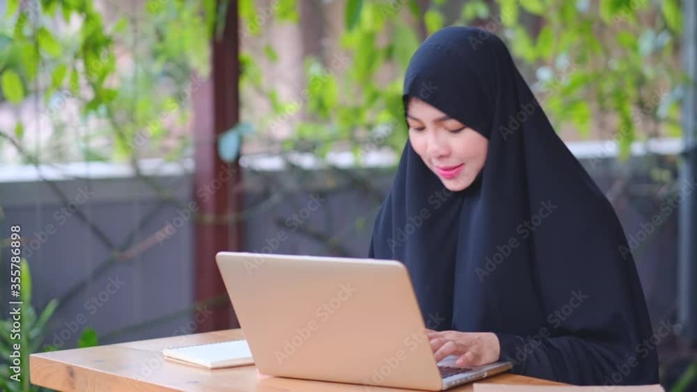 Muslim girl work from home with laptop, she show greeting to co-worker via online meeting then write information on to notebook. Concept of new normal lifestyle for working and stay at home. Muslim girl work from home with laptop, she show greeting to co-worker via online meeting then write information on to notebook. Concept of new normal lifestyle for working and stay at home.