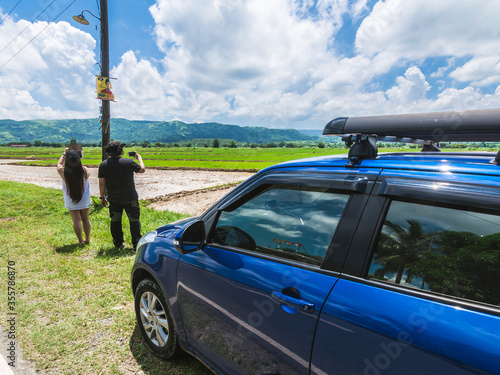 A couple that parked their car by the road to take landscape pictures. Flat plains and distant mountain range in Nueva Ecija, Philippines. photo