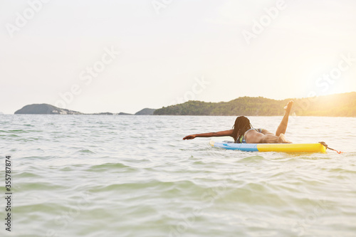 Black young woman swimming on sup board in the ocean in rayS of declining sun photo