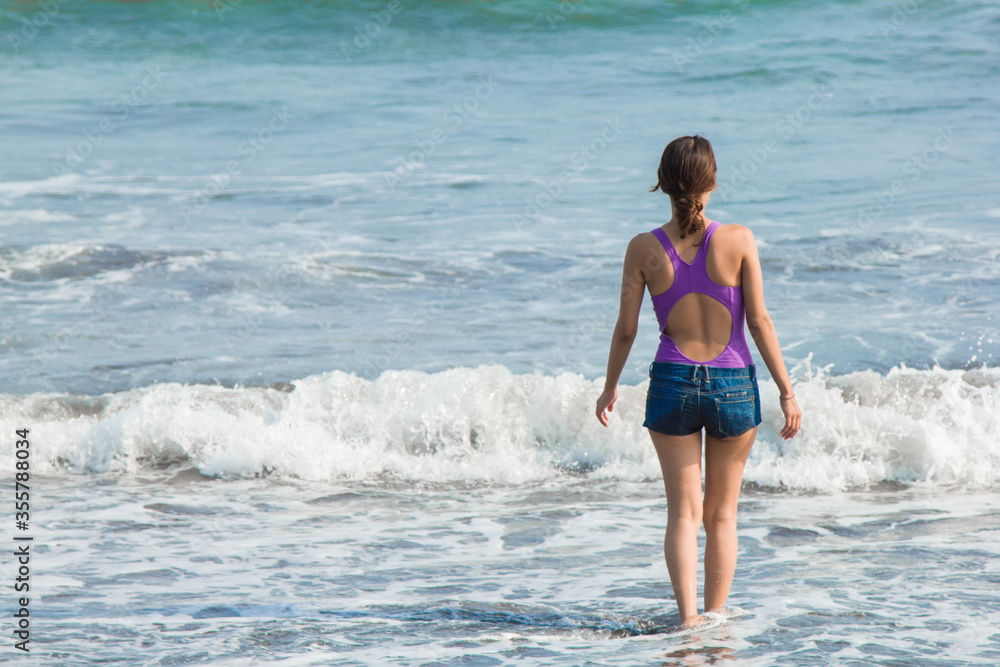 young woman in purple bikini walking among the waves young woman in purple bikini walking among the waves