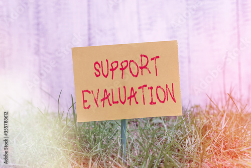 Writing note showing Support Evaluation. Business concept for helps evaluate a subjects worth or significances Plain paper attached to stick and placed in the grassy land photo