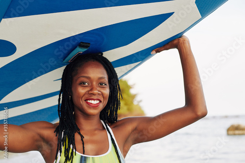 Portrait of happy wet young Black woman carrying surfboard over her head photo