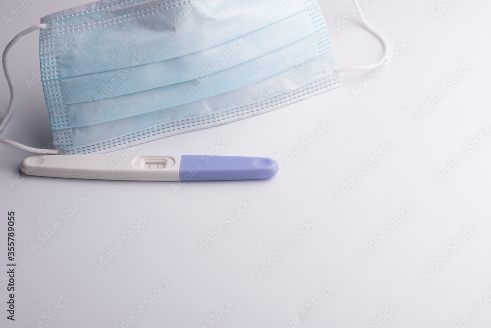 A pregnancy test kit with medical face mask,isolated over various background,conception during pandemic concept A pregnancy test kit with medical face mask,isolated over various background,conception during pandemic concept