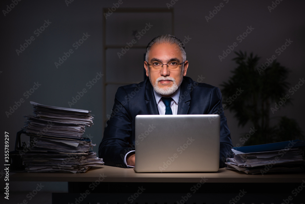 Old male employee working late at workplace Old male employee working late at workplace
