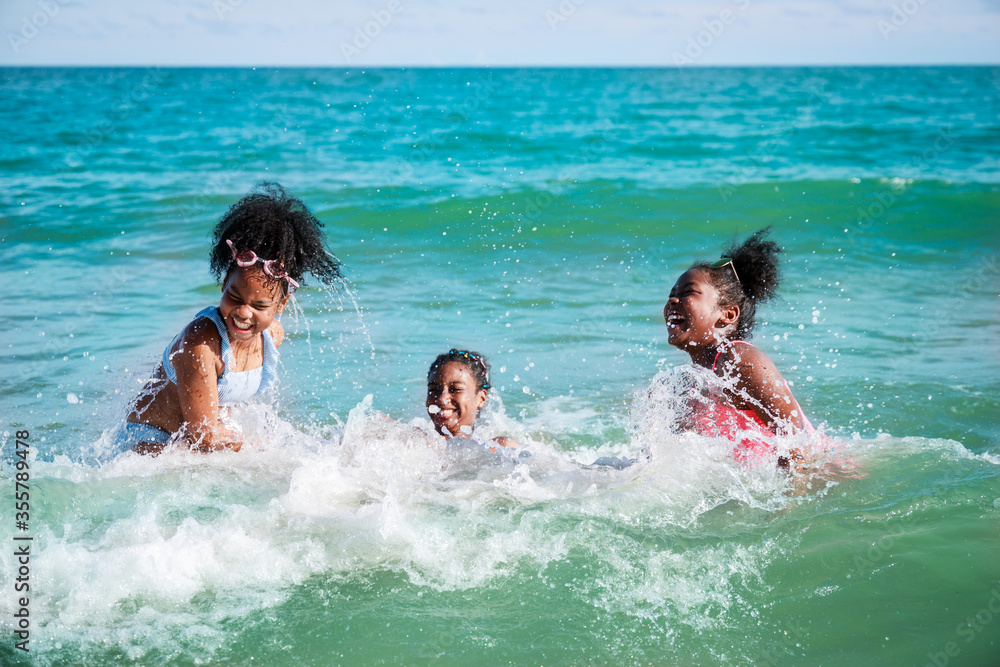 Happy three African American kids are swimming in the sea playfully together. With waves and splashes of water. Happy friendship. Happy vacation holiday. Relaxation in vacation in the summer concept.