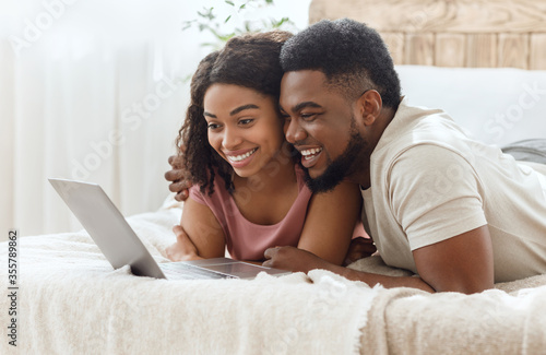 Black couple in love surfing internet together, lying on bed