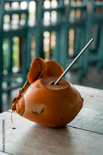 Fresh organic king coconut water served with reusable metallic straw on wooden table at cafe. Summer drink. Sri Lanka tropical beverage. Eco-friendly cafe. Copy space