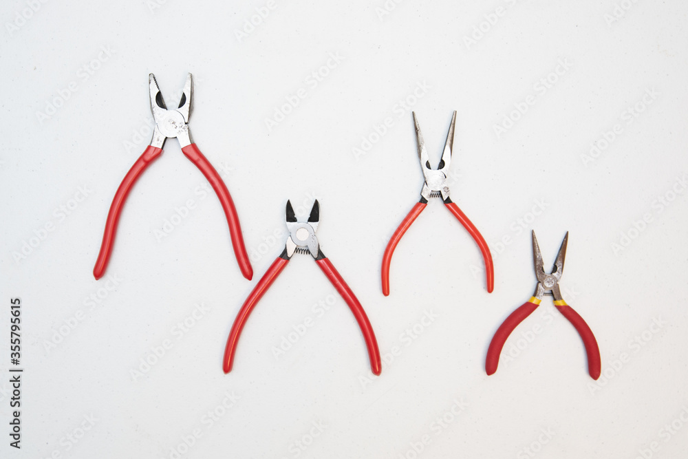 Different sizes of red pliers on a wooden background. Top view of repairing work tools on a wooden table. Different sizes of red pliers on a wooden background. Top view of repairing work tools on a wooden table.