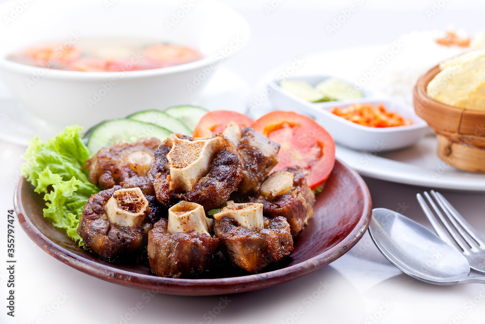 Fried oxtail with soup and white rice, chili sauce, lime, chips. Served on a plate decorated with tomatoes, cucumbers, lettuce. Fried oxtail with soup and white rice, chili sauce, lime, chips. Served on a plate decorated with tomatoes, cucumbers, lettuce.