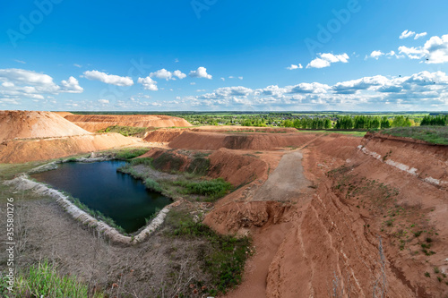 Abandoned sand pit with a lake on a background of blue sky with clouds.