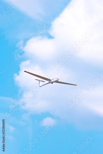 Small glider flying against the blue sky and clouds