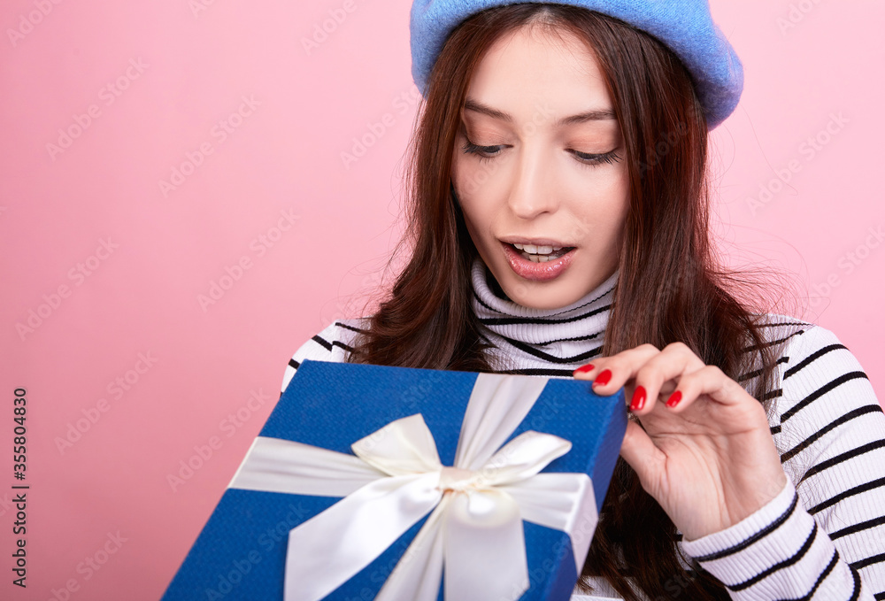 Portrait of a French woman in a fashionable beret hat in glasses with a gift in her hands on a pink background. Portrait of a French woman in a fashionable beret hat in glasses with a gift in her hands on a pink background.