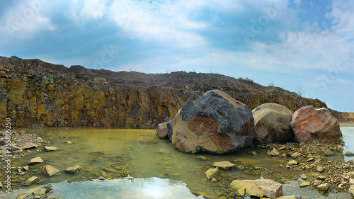Large boulders in muddy water and rocky cliff on background