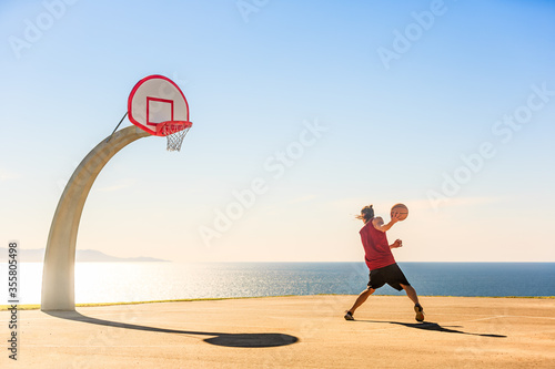 Obraz na plátne Basketball player dribbling the basket ball outdoor on a sunny day with beautiful ocean view in the background