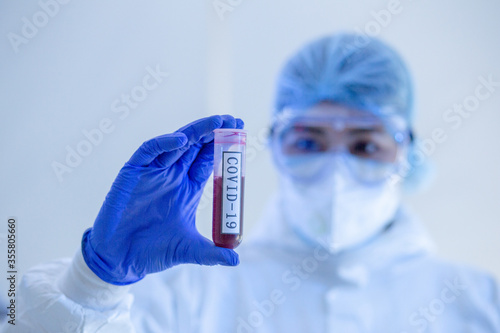 Focus on Blood test tube of COVID19, Coronavirus or Novel corona virus epidemic disease. Lab technician scientist in PPE Personal Protective Equipment holding blood tube test in hospital laboratory.