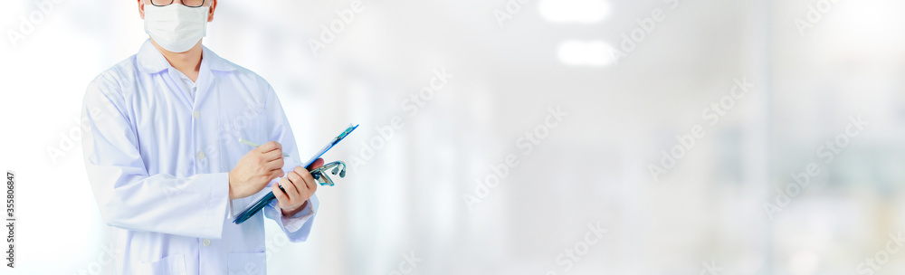 Portrait of Asian medical male Doctor wear a mask to prevent germs and standing in front of his blurred interior hallway in hospital banner background.Concept of effective work in hospitals. Portrait of Asian medical male Doctor wear a mask to prevent germs and standing in front of his blurred interior hallway in hospital banner background.Concept of effective work in hospitals.