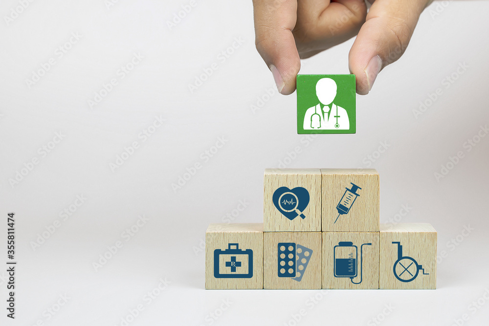 Hand picking up doctor icon on cube wooden toy blocks with medical icons stacked. Concepts of illness treatment and health insurance. Hand picking up doctor icon on cube wooden toy blocks with medical icons stacked. Concepts of illness treatment and health insurance.
